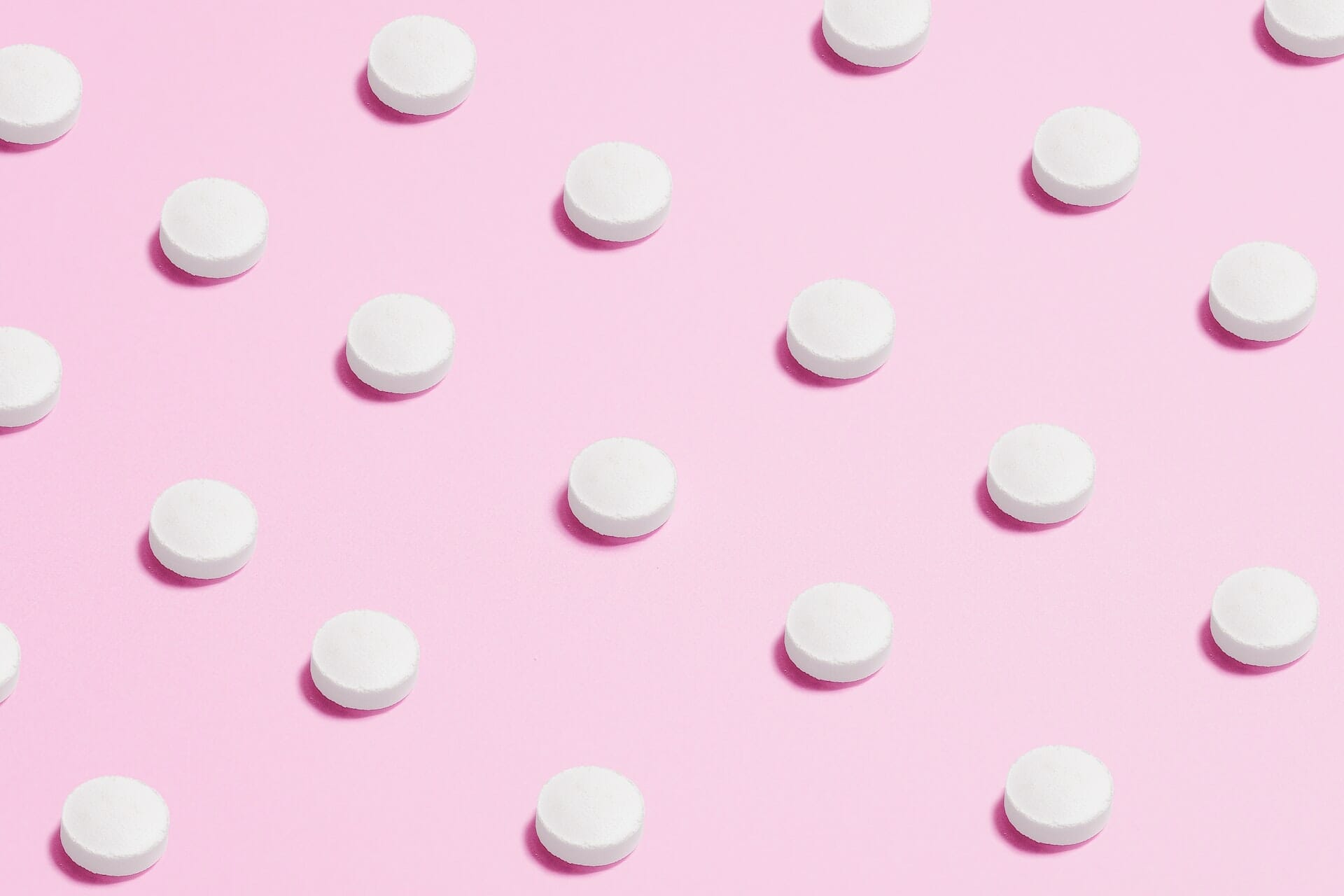 Small, round white pills on a pink background