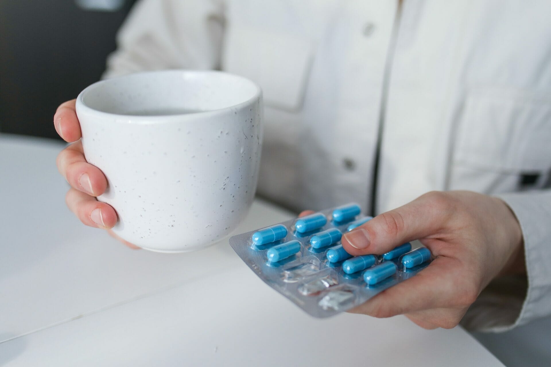 A person holding a cup and a packet of medication